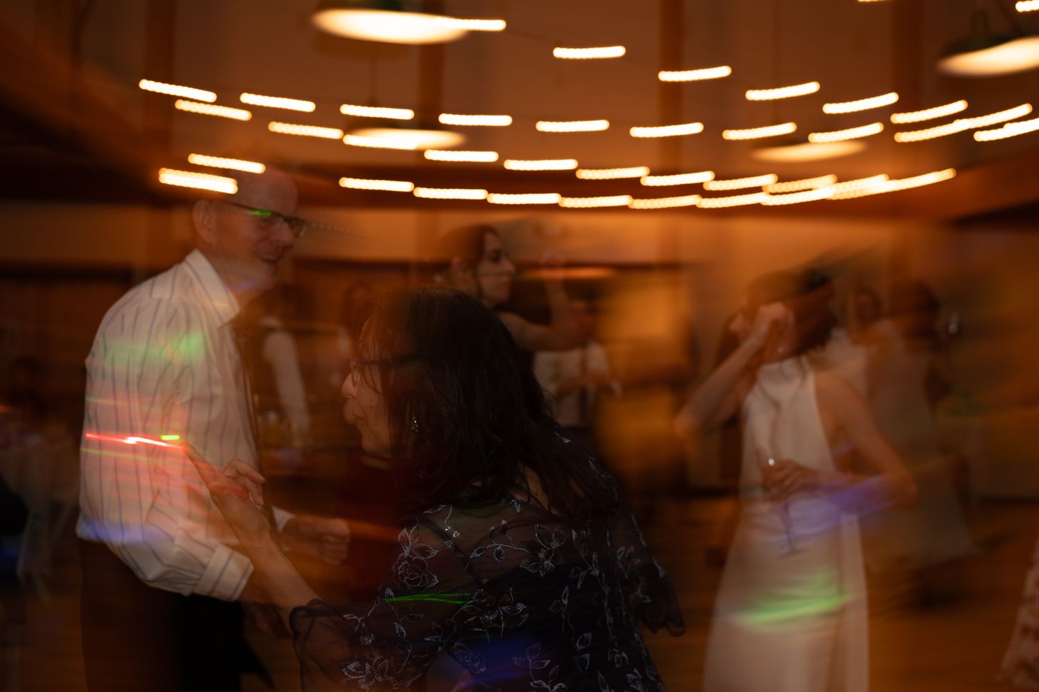 Motion-blurred dancers under warm ceiling lights create an atmospheric party scene.