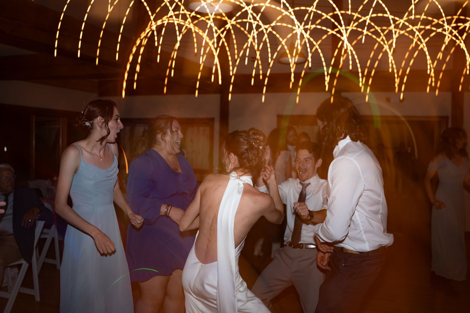 People dancing under decorative string lights at an evening celebration.