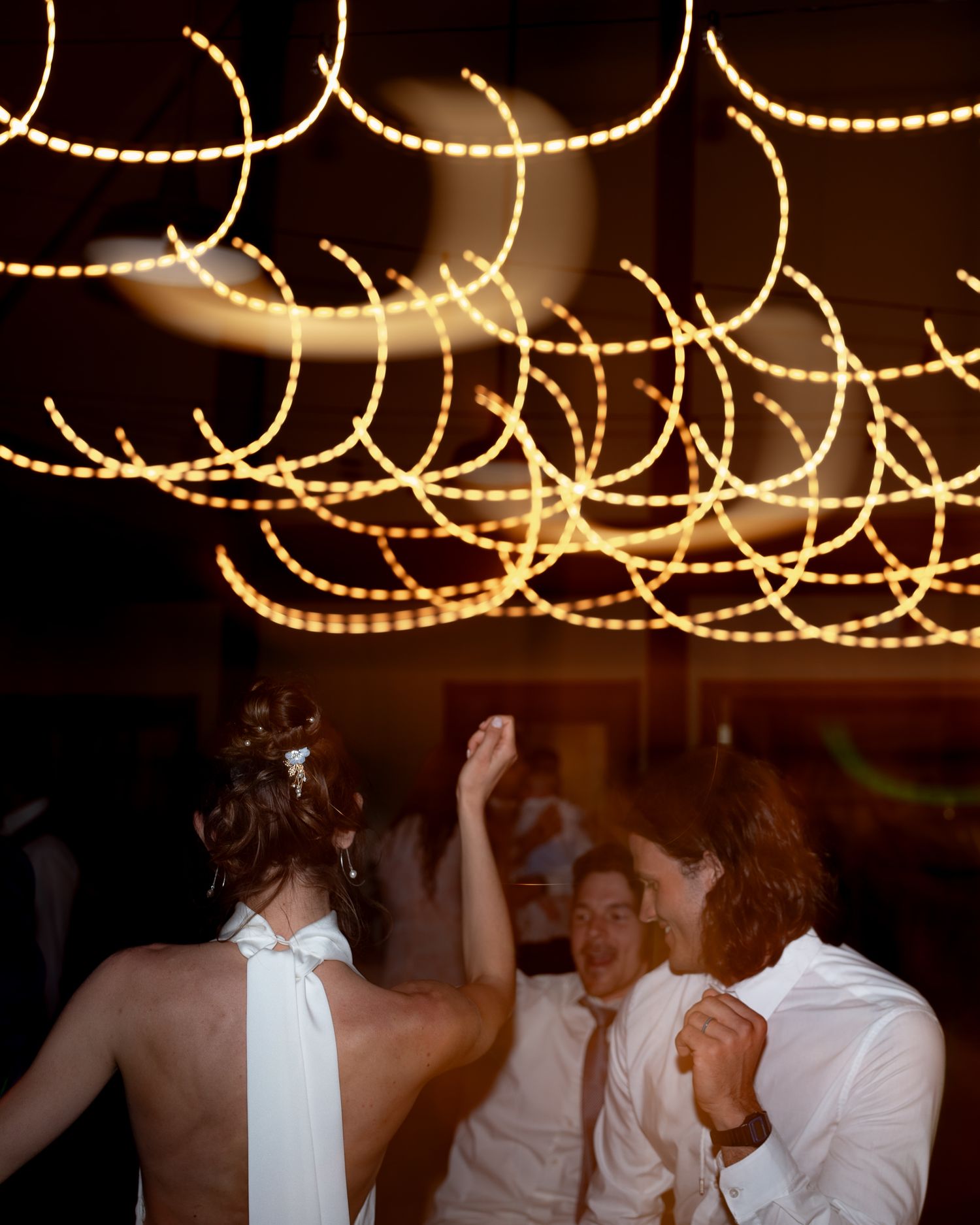 Dancers celebrate under illuminated string lights creating sweeping patterns overhead.