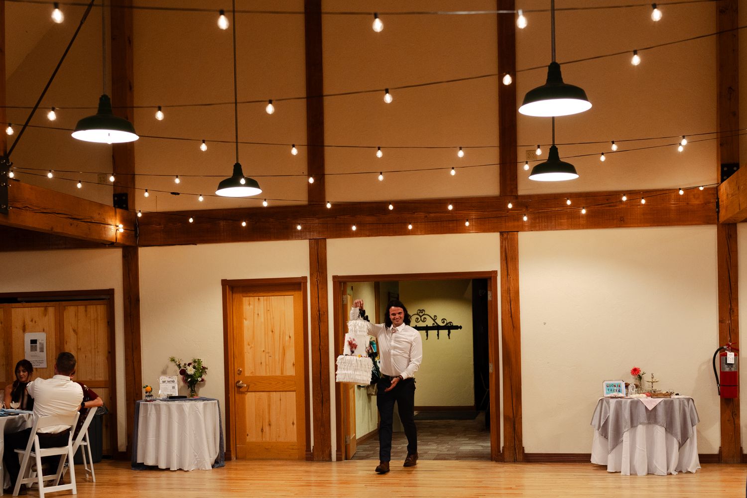 Wedding reception venue with string lights and pendant lamps hanging from wooden beams.