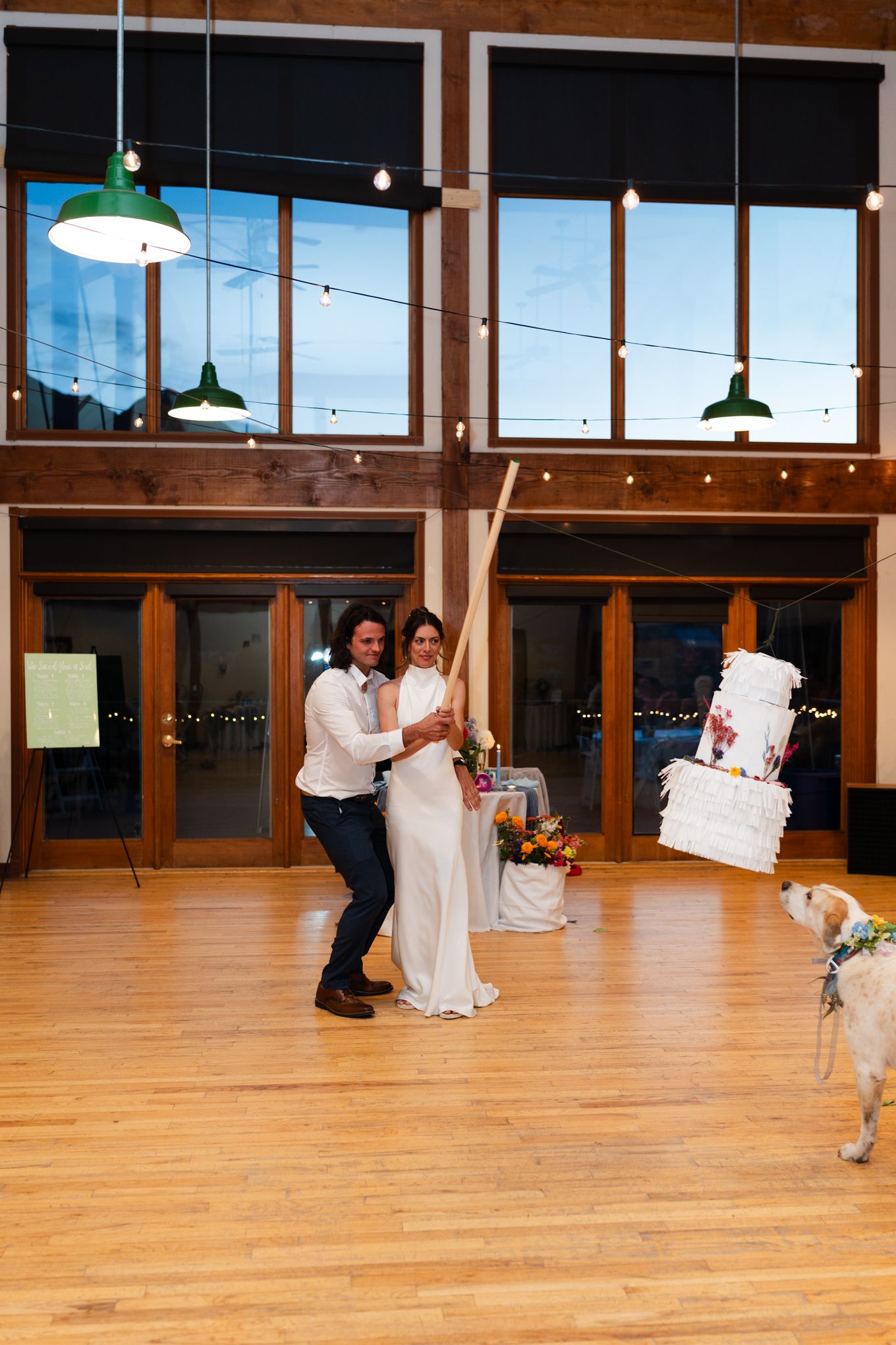 Couple dancing in a reception hall with floor-to-ceiling windows and suspended green pendant lights.