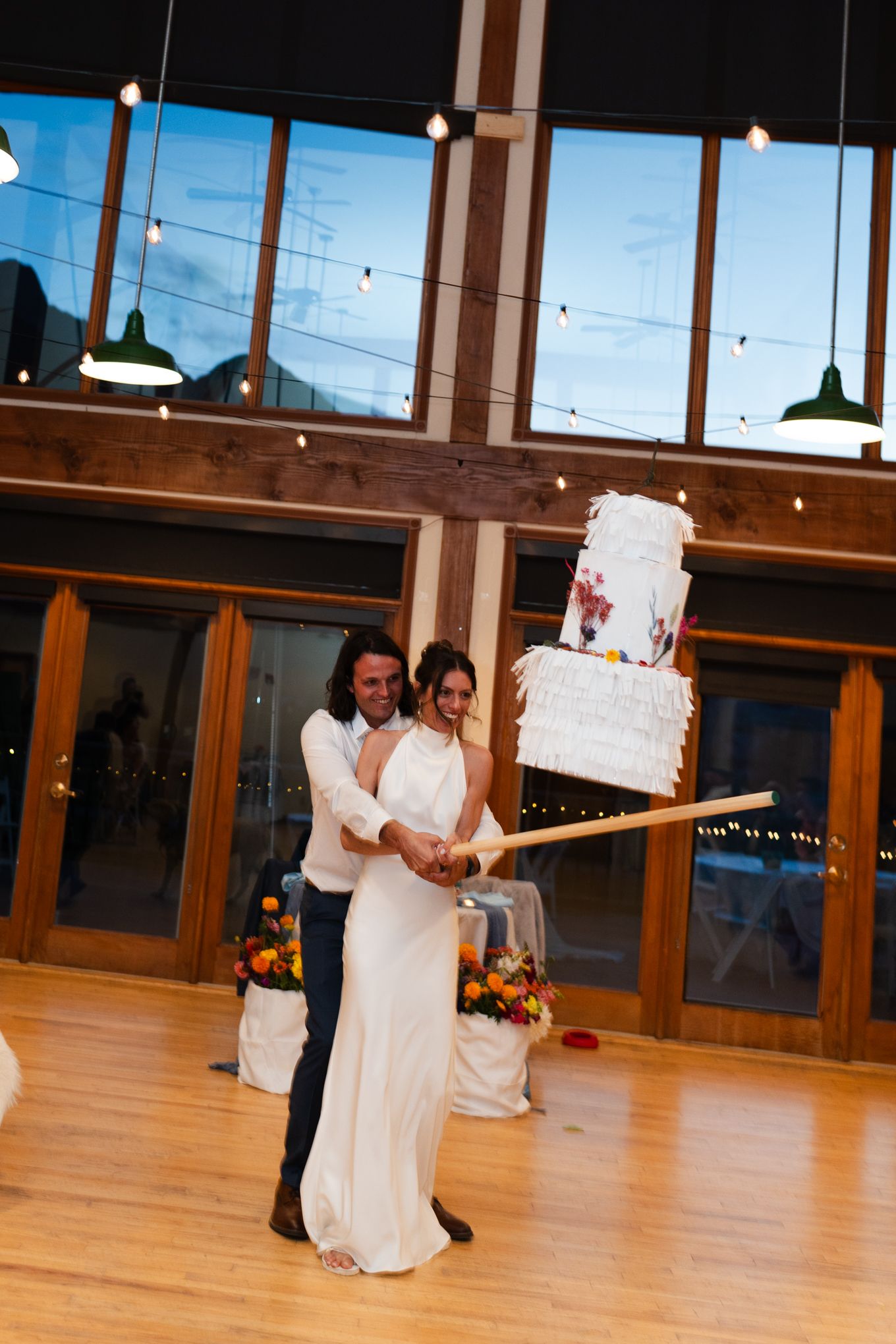 Couple working together to lift their wedding cake with a long pole in an elegant reception venue.