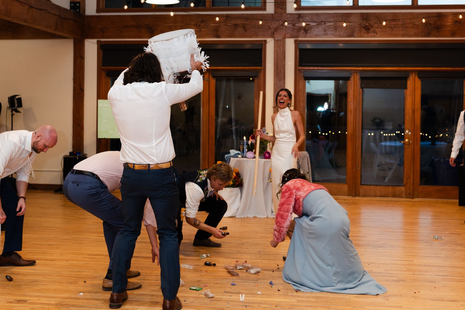 Wedding guests playfully clean up cake pieces from hardwood floor.