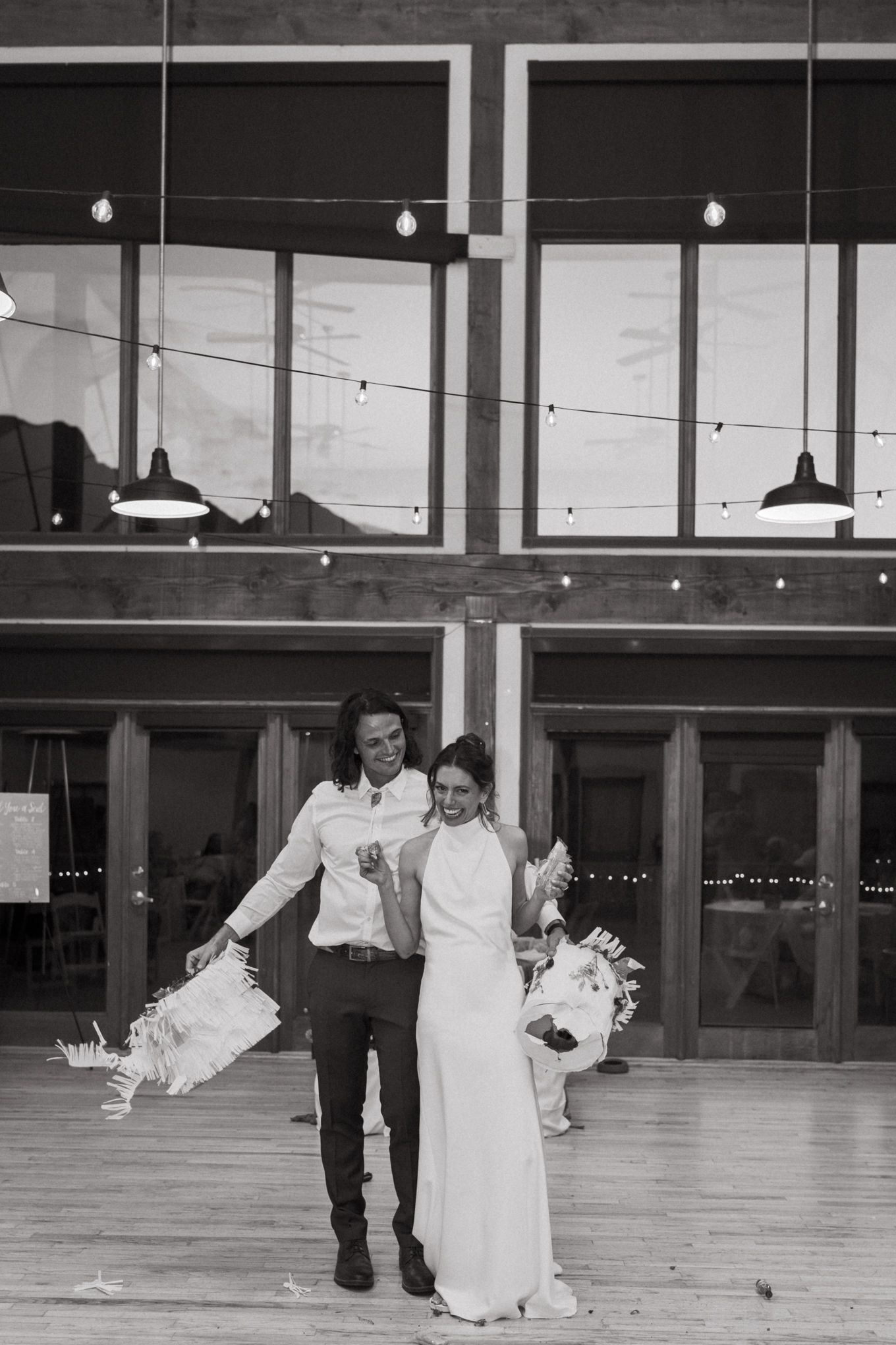 Black and white wedding photo in a venue with string lights and large windows.