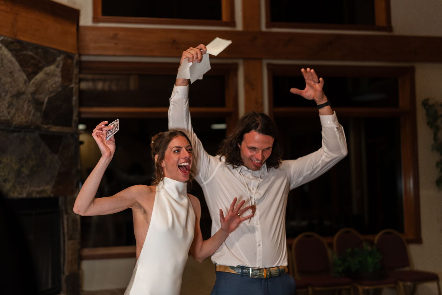 A couple dances joyfully together with raised arms at an indoor celebration.