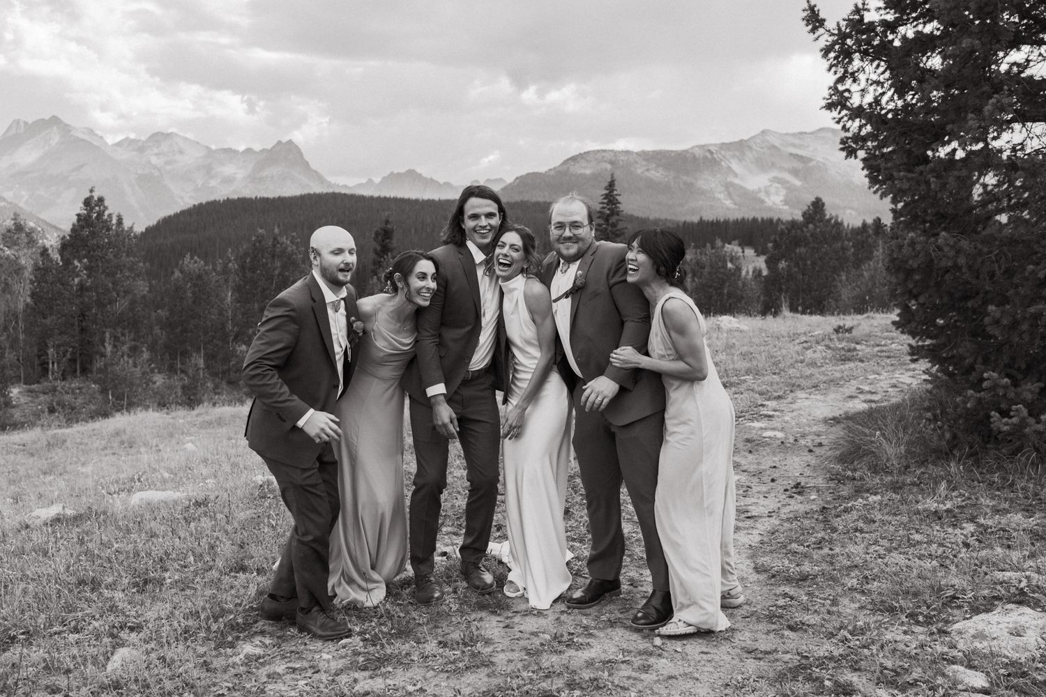 Wedding party poses for black and white group photo with mountain backdrop.