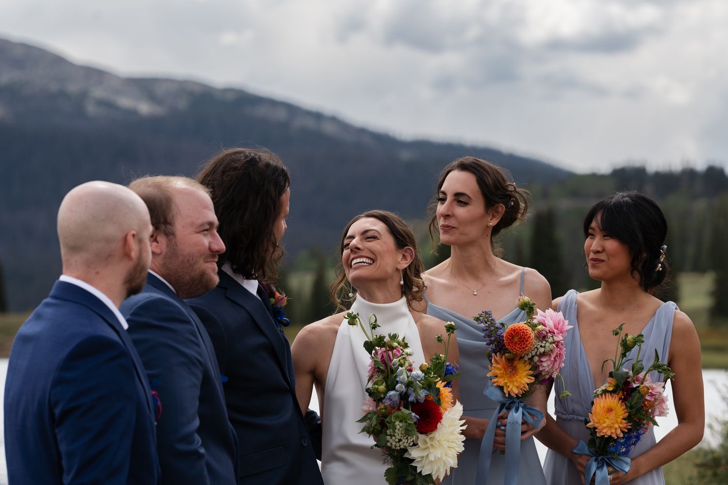 Wedding party shares a lighthearted moment together in front of mountain scenery.