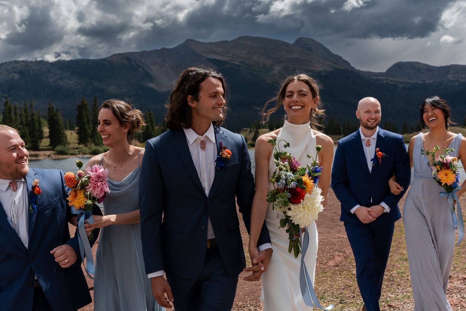 Wedding party walks together against dramatic mountain landscape.