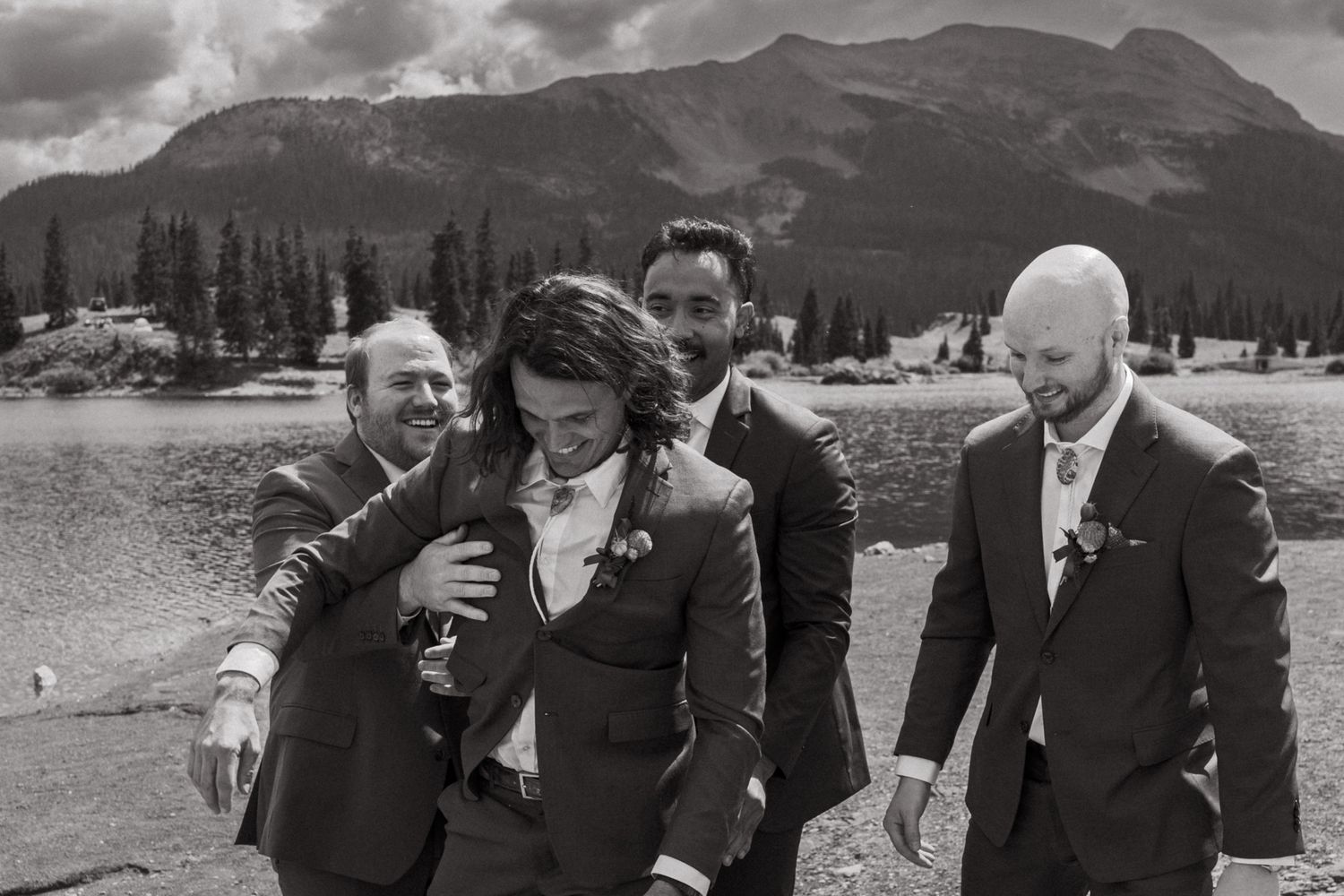 Black and white candid shot of wedding party laughing together outdoors.