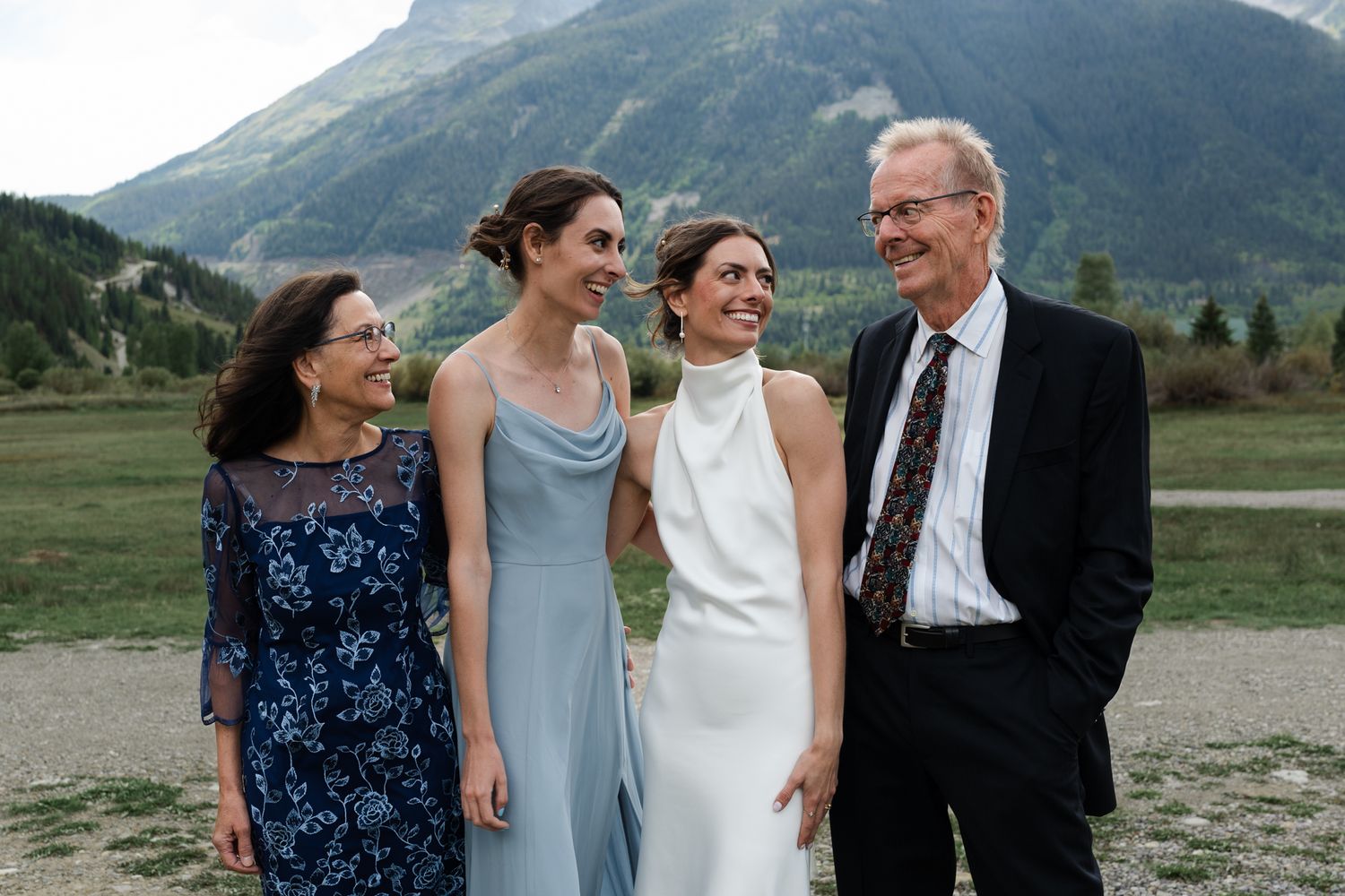 Happy wedding group shares laughs together against stunning mountain backdrop.