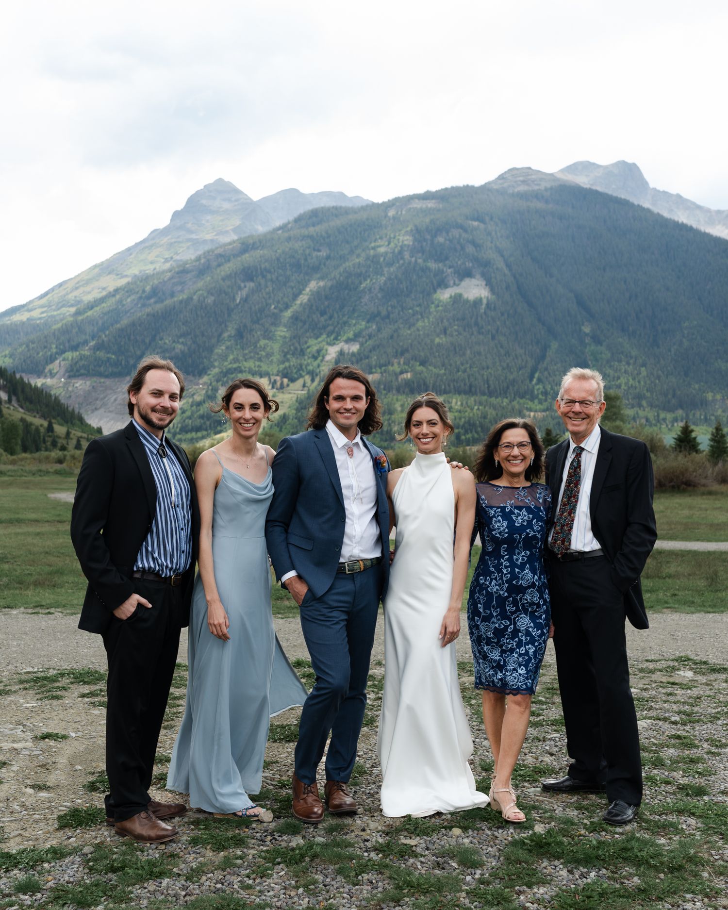 Wedding party of six poses together in front of mountain scenery.
