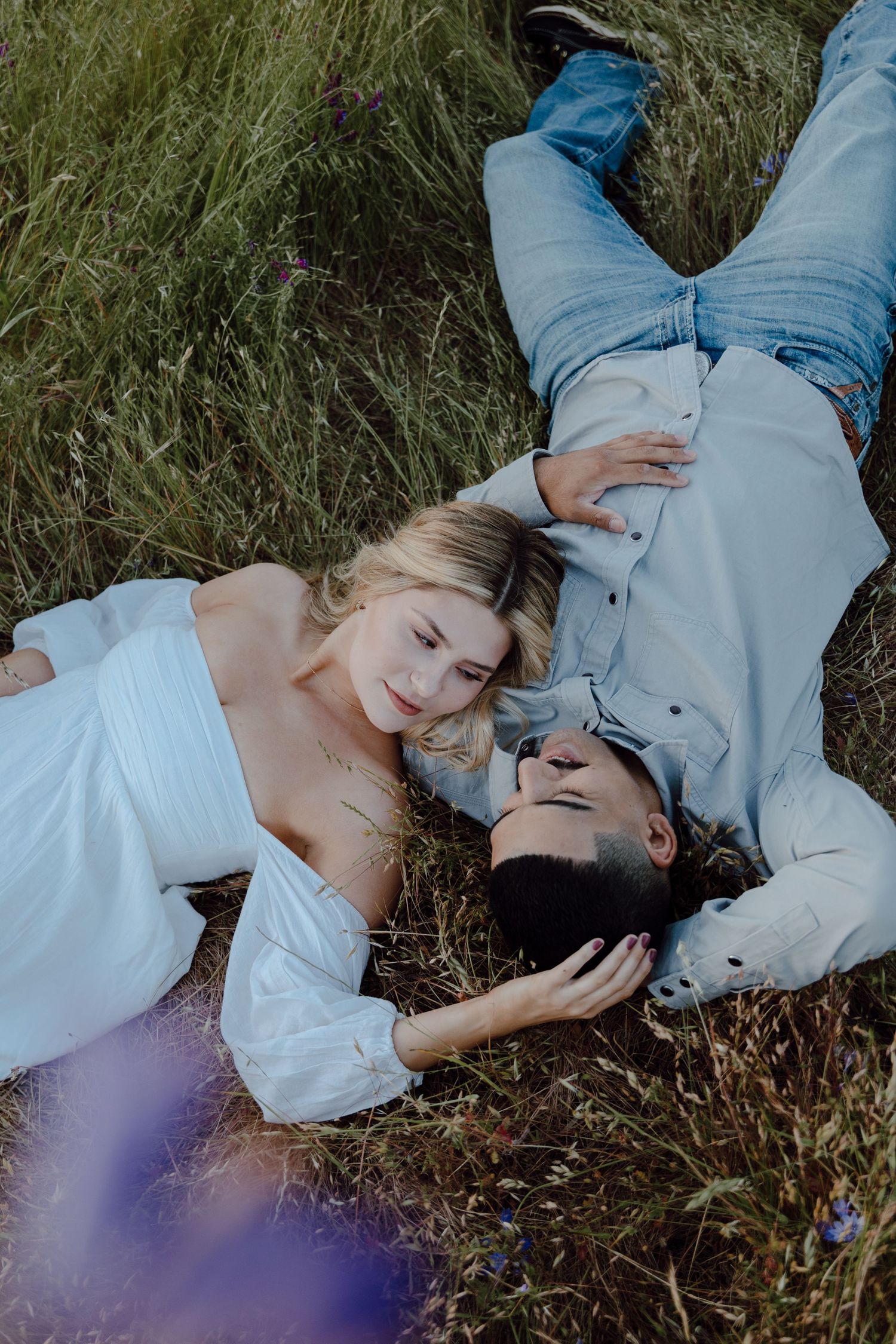 Couple laying in tall grass together during golden hour in a romantic countryside setting.