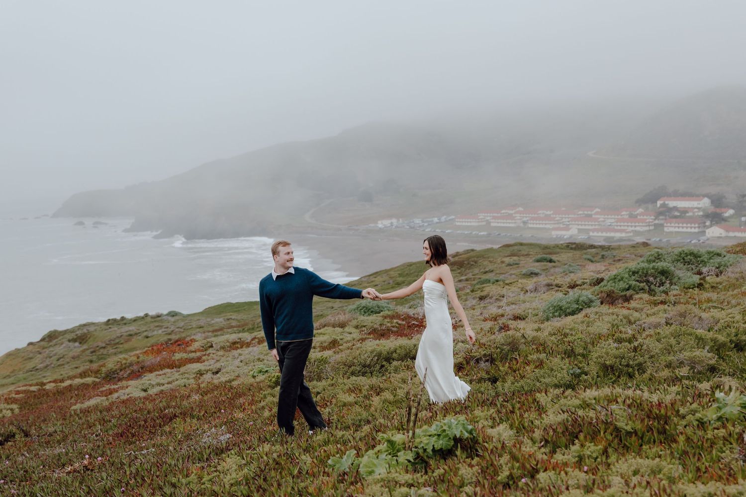 A couple poses together on white marble steps of a classical stone portico surrounded by greenery.