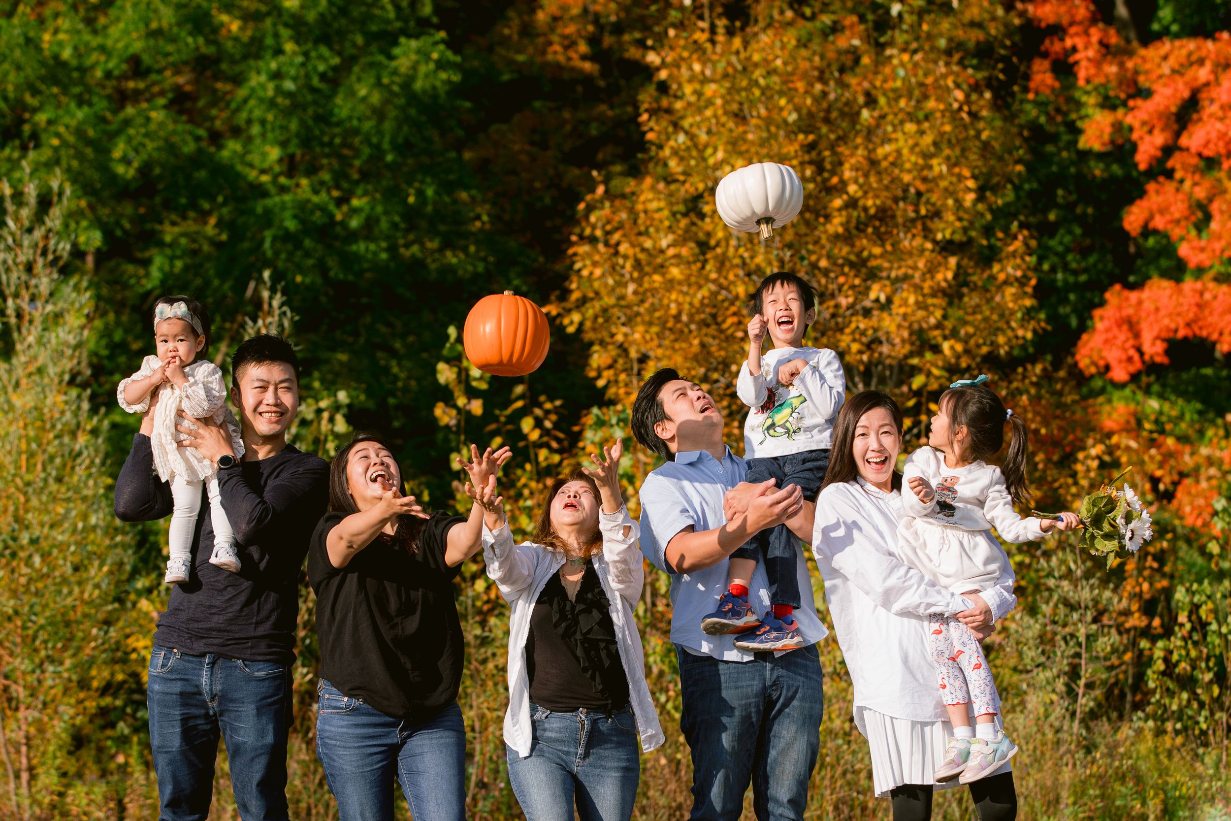Group tossing pumpkins in the air with autumn foliage creating a colorful seasonal backdrop in nature.