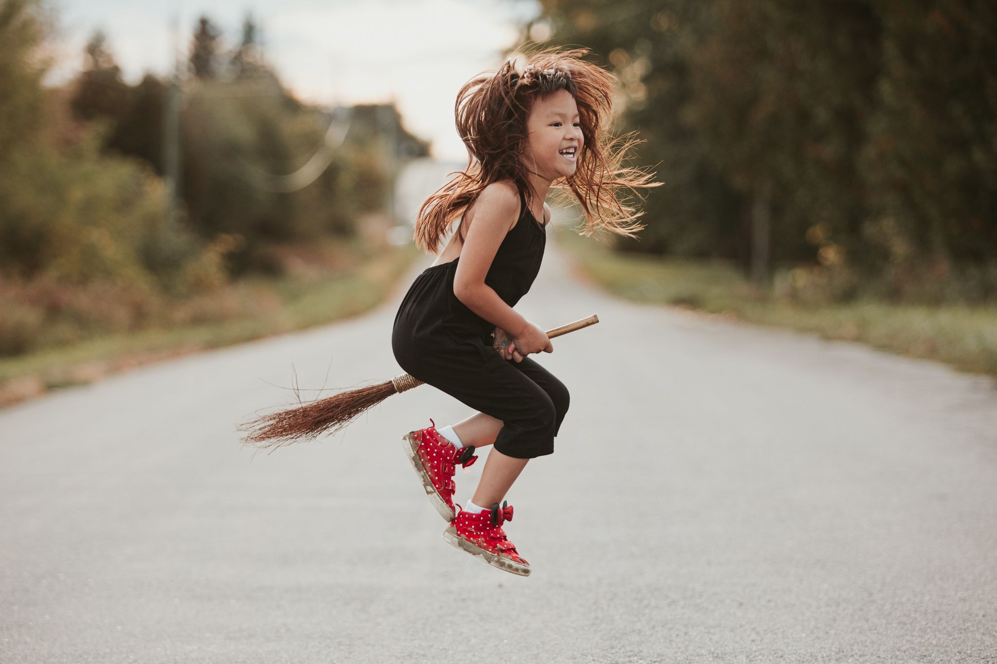 Child in black outfit jumping playfully on a road wearing red roller skates with hair flowing in the wind.