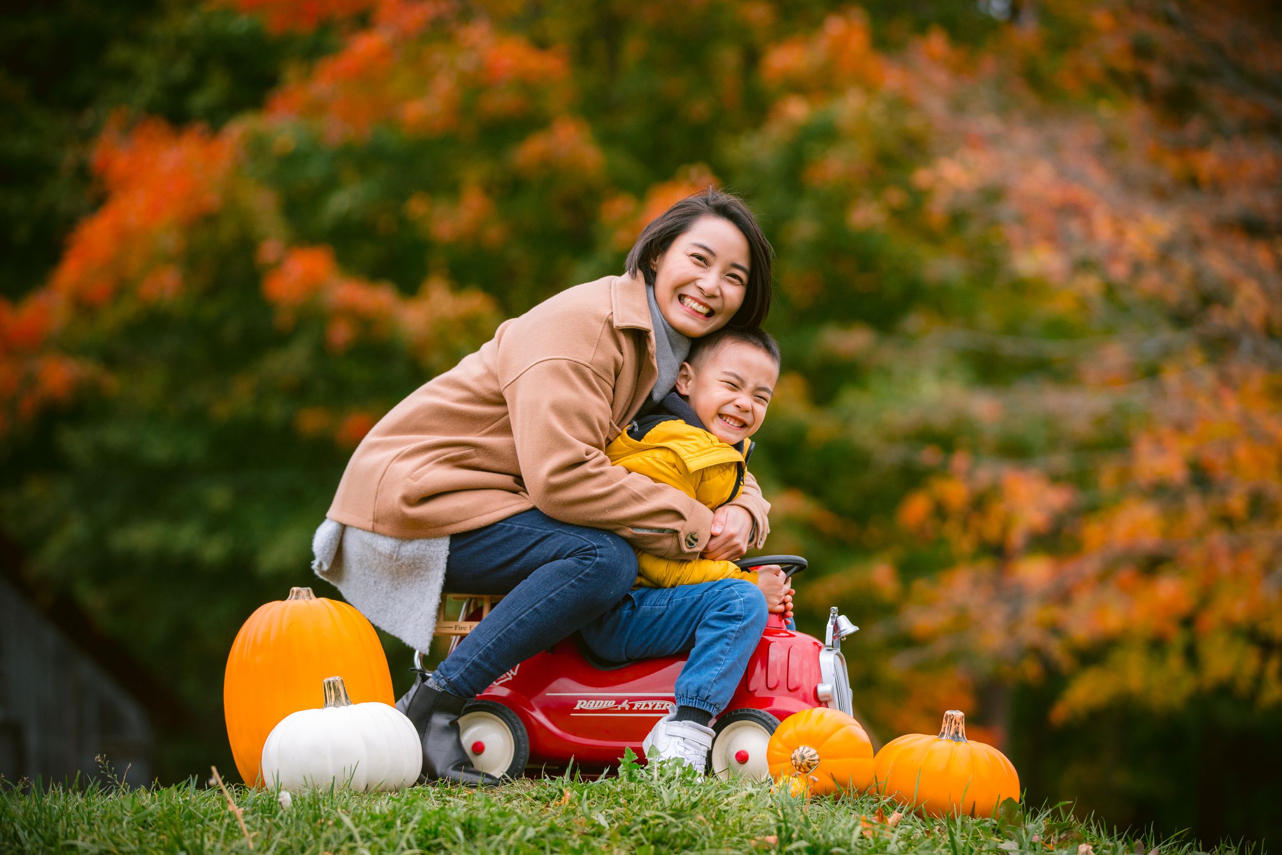A fun autumn scene with pumpkins and a child sitting on a red wagon outdoors with beautiful fall foliage in the background.