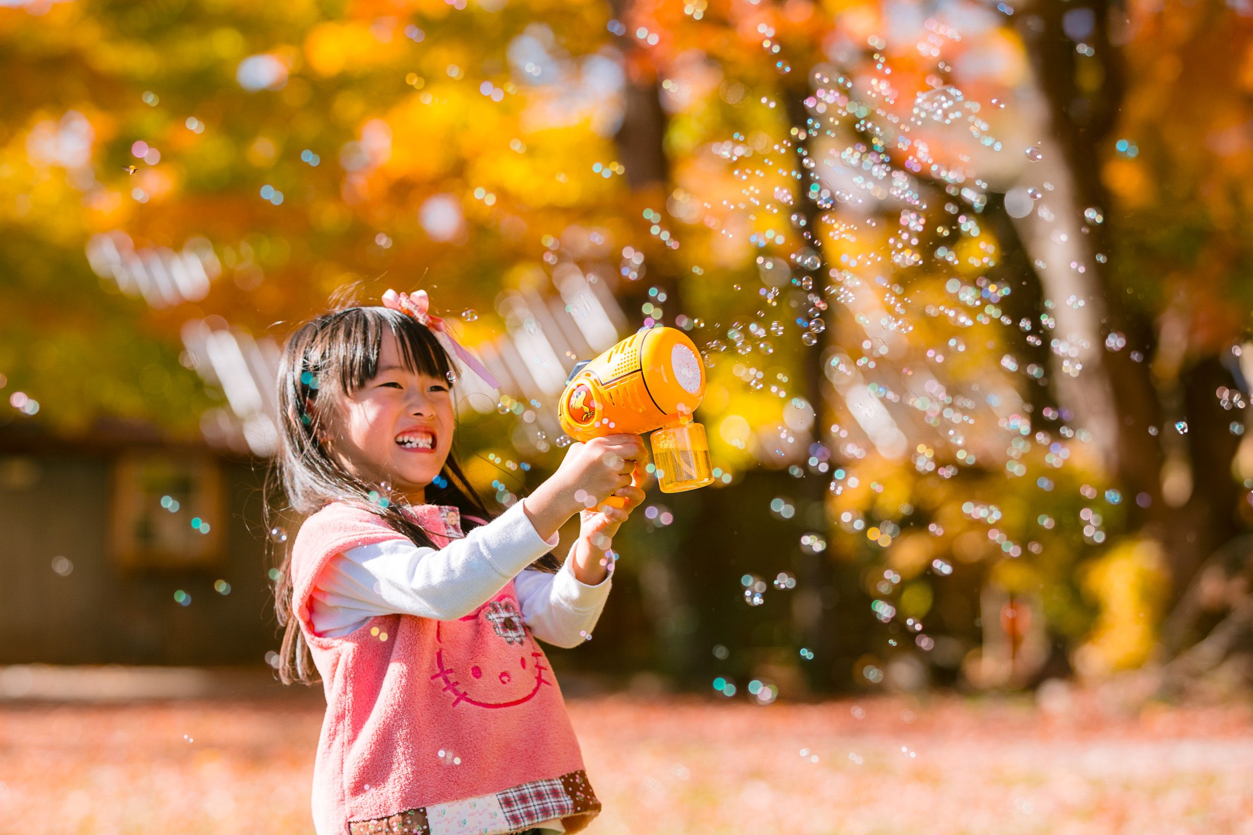 Someone in a pink sweater plays with falling autumn leaves on a bright sunny fall day.