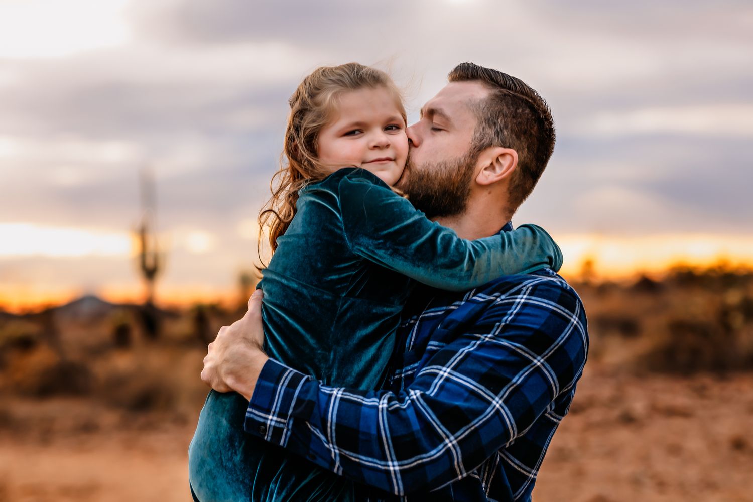 A loving embrace between dad and child silhouetted against an Arizona desert sunset with saguaro cactus in the background.
