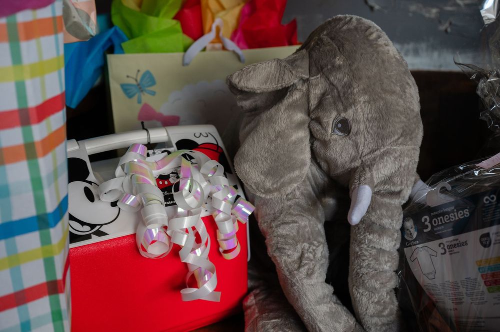 A large gray stuffed elephant plush toy sits next to smaller white plush toys on a colorful striped surface.