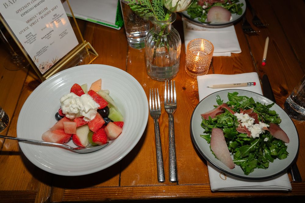 Two elegant plates featuring watermelon and feta salad alongside mixed greens on a wooden table with candlelight.