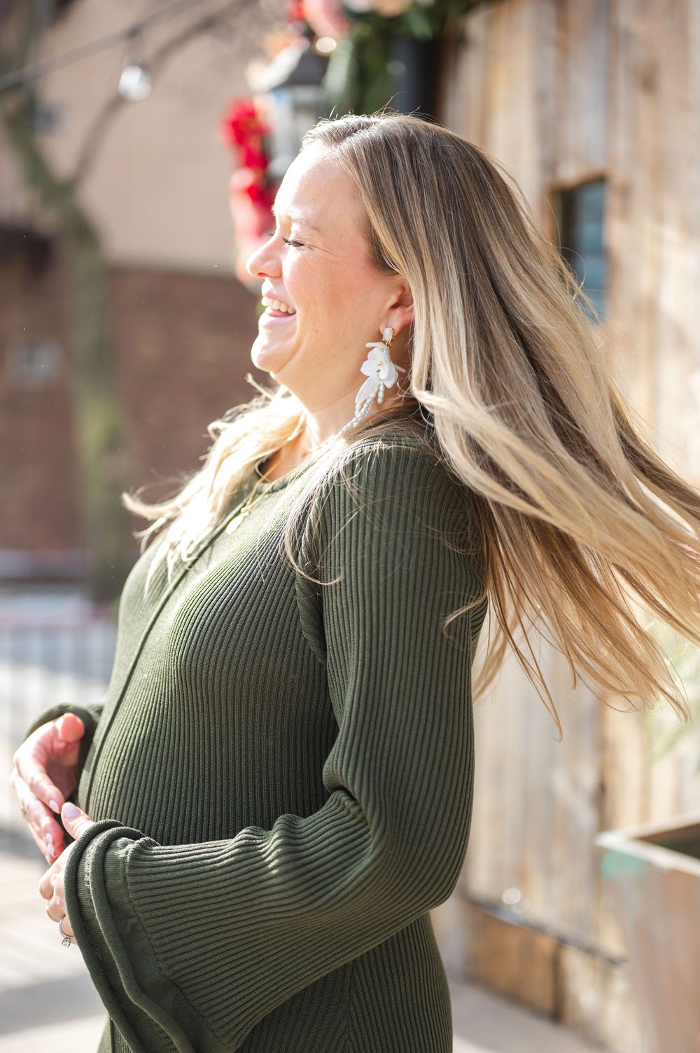 A woman in a green sweater laughs joyfully as her blonde hair flows in the wind.