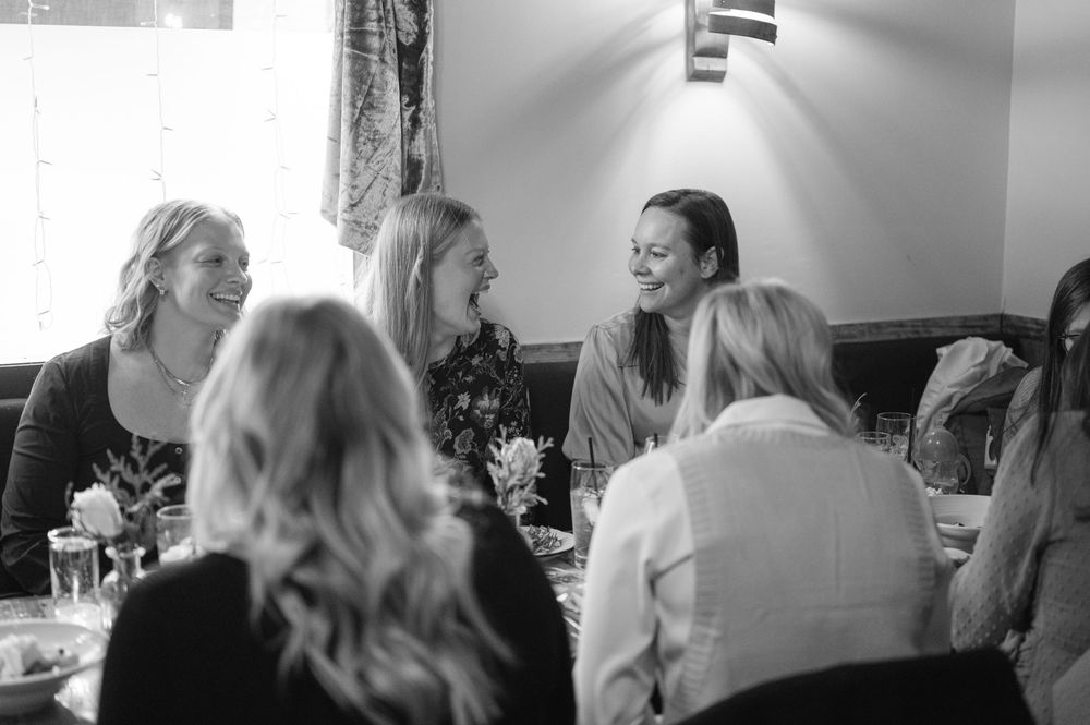 A group of people share laughter and conversation around a table at a social gathering in black and white photography.