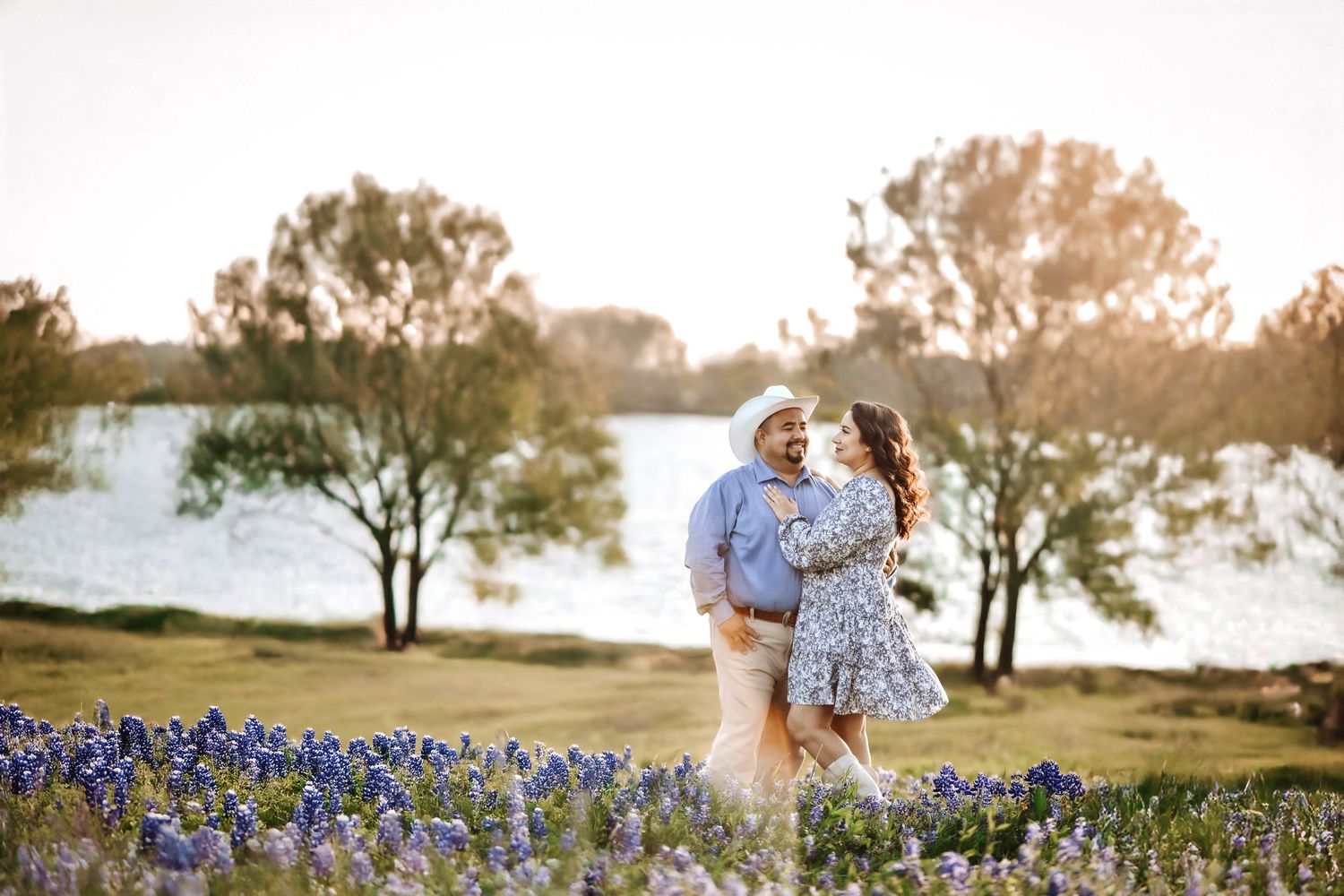 Couple walking hand in hand through a field of blooming bluebonnets near the lake at Ennis Bluebonnet Trail