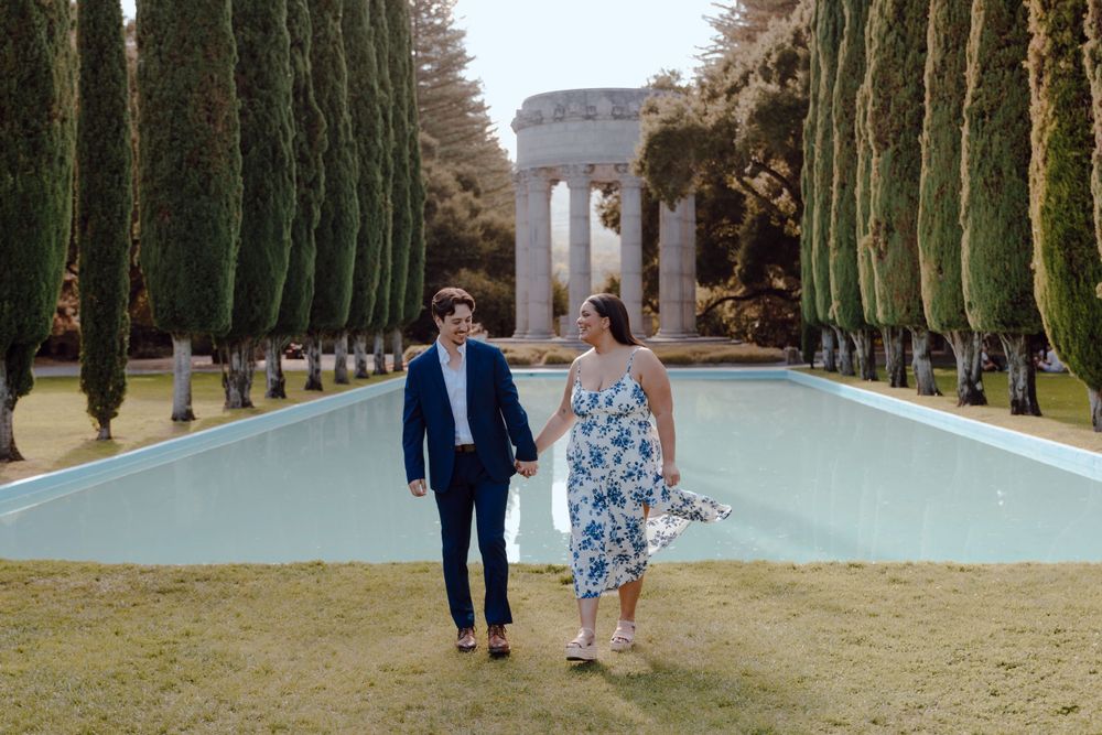Couple walking hand in hand along a reflecting pool lined with cypress trees leading to a memorial monument.