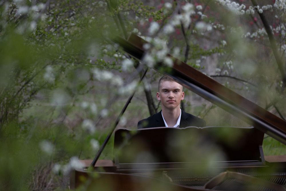 A piano player sits at a grand piano outdoors surrounded by delicate cherry blossoms in spring.
