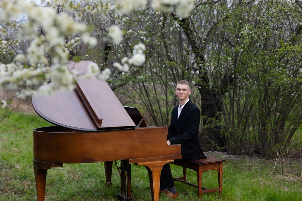 Professional pianist performs outdoors next to blooming white spring trees with a grand piano in nature setting.