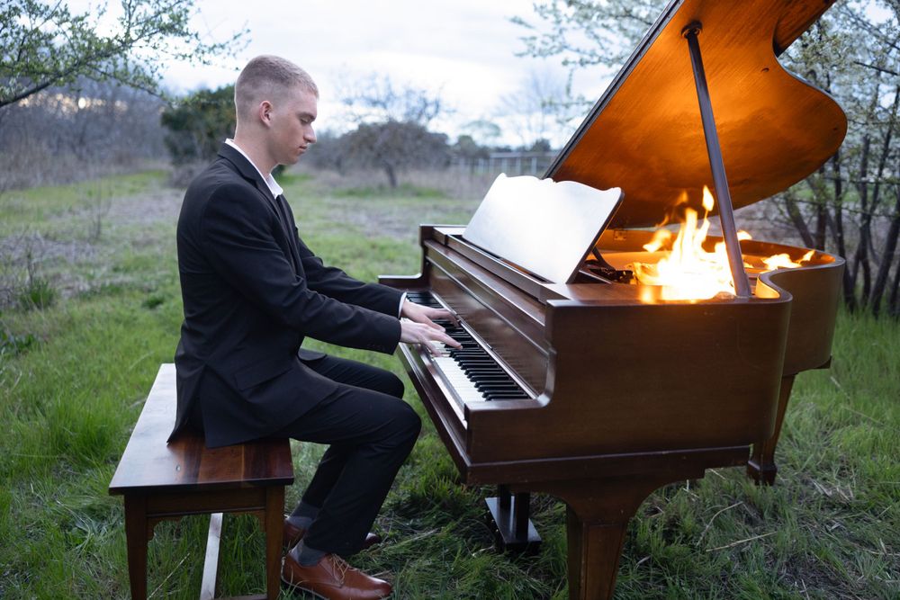 Pianist performs outdoors on grand piano at dusk with warm lighting illuminating the instrument.