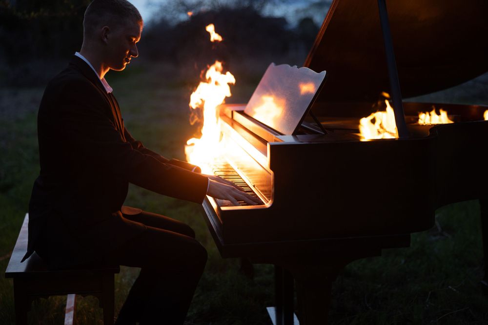 A grand piano is illuminated by glowing lanterns in a darkened evening setting, creating a dramatic scene.