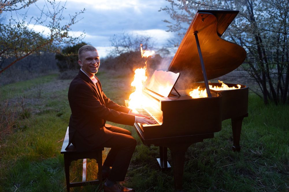 A fiery outdoor performance with a grand piano ablaze in flames against a twilight sky during sunset.