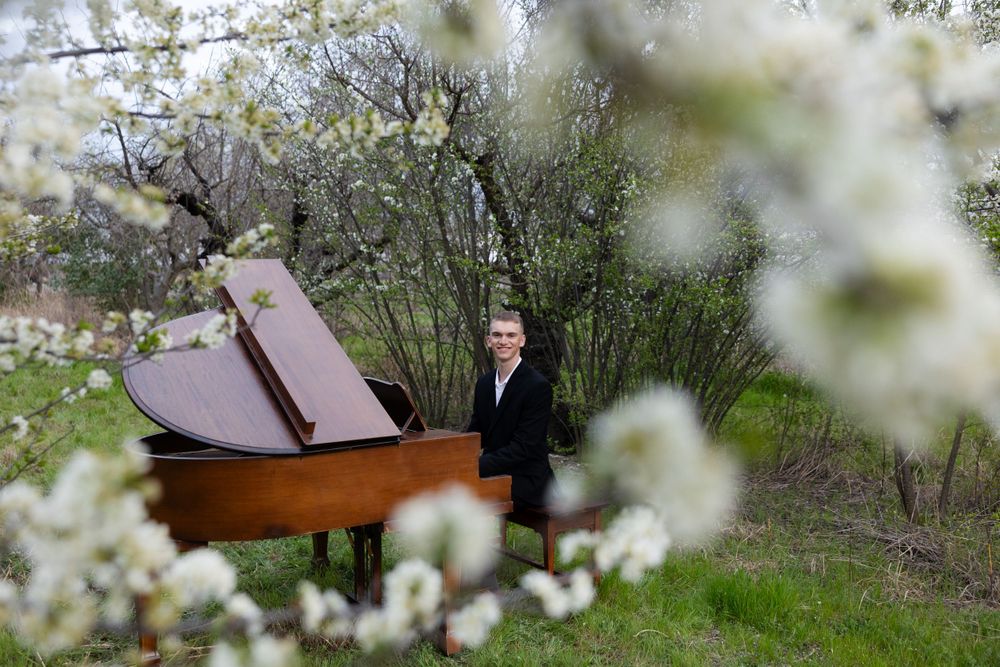A grand piano sits among blooming white spring flowers and trees on a grassy hillside.