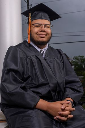 Graduate in cap and gown sits on steps during commencement.