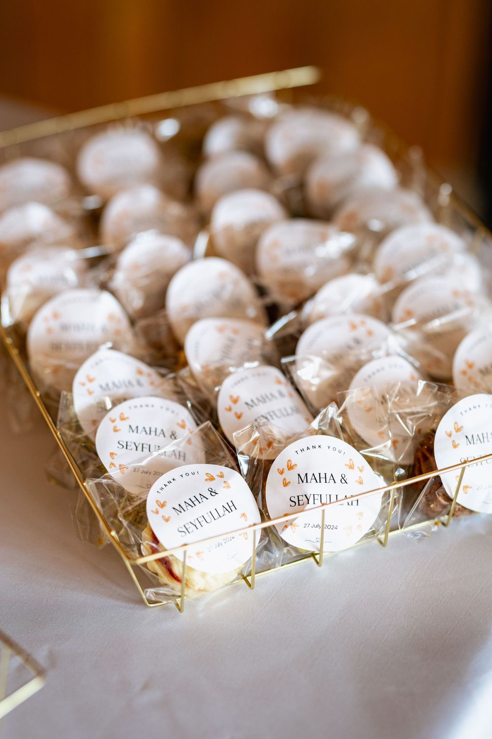 White powdered wedding favor cookies arranged in a gold tray with personalized name tags.