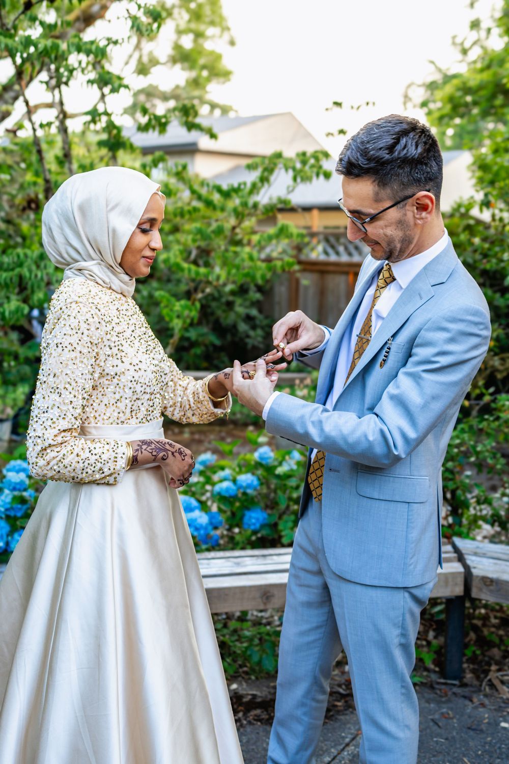A couple in wedding attire share a moment in a garden with blue hydrangeas in the background.