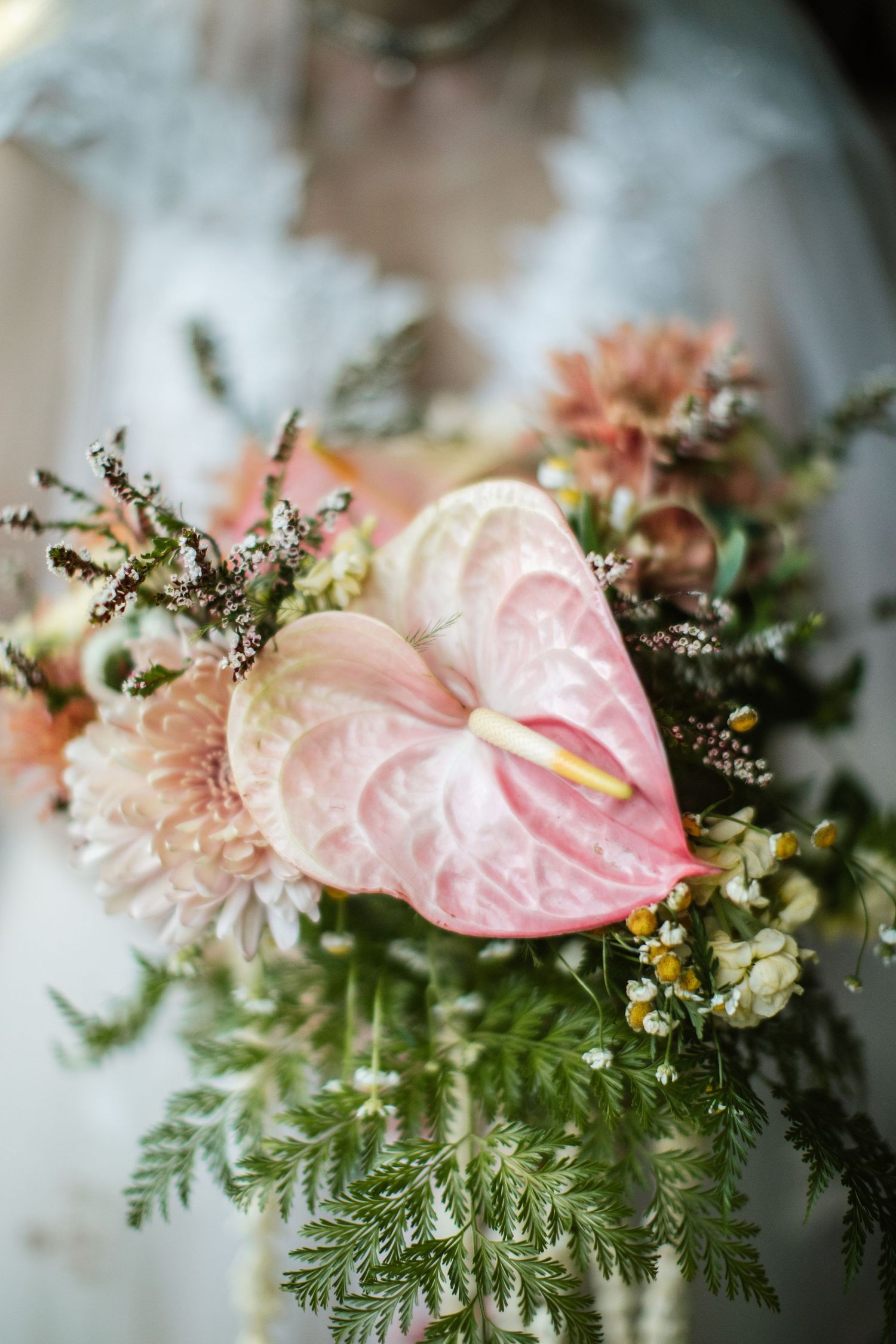 Close-up of a delicate pink anthurium and coral flowers with ferns in a romantic wedding bouquet arrangement.