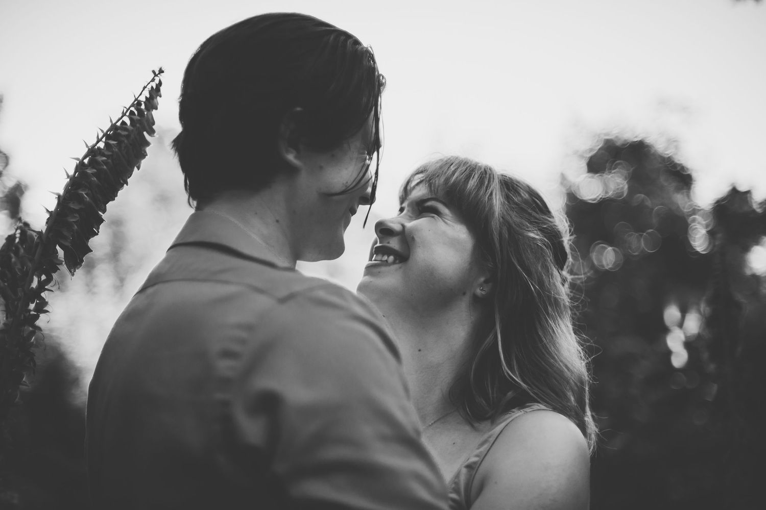 A couple shares a tender moment, gazing into each other's eyes with smiles, captured in soft, natural light.