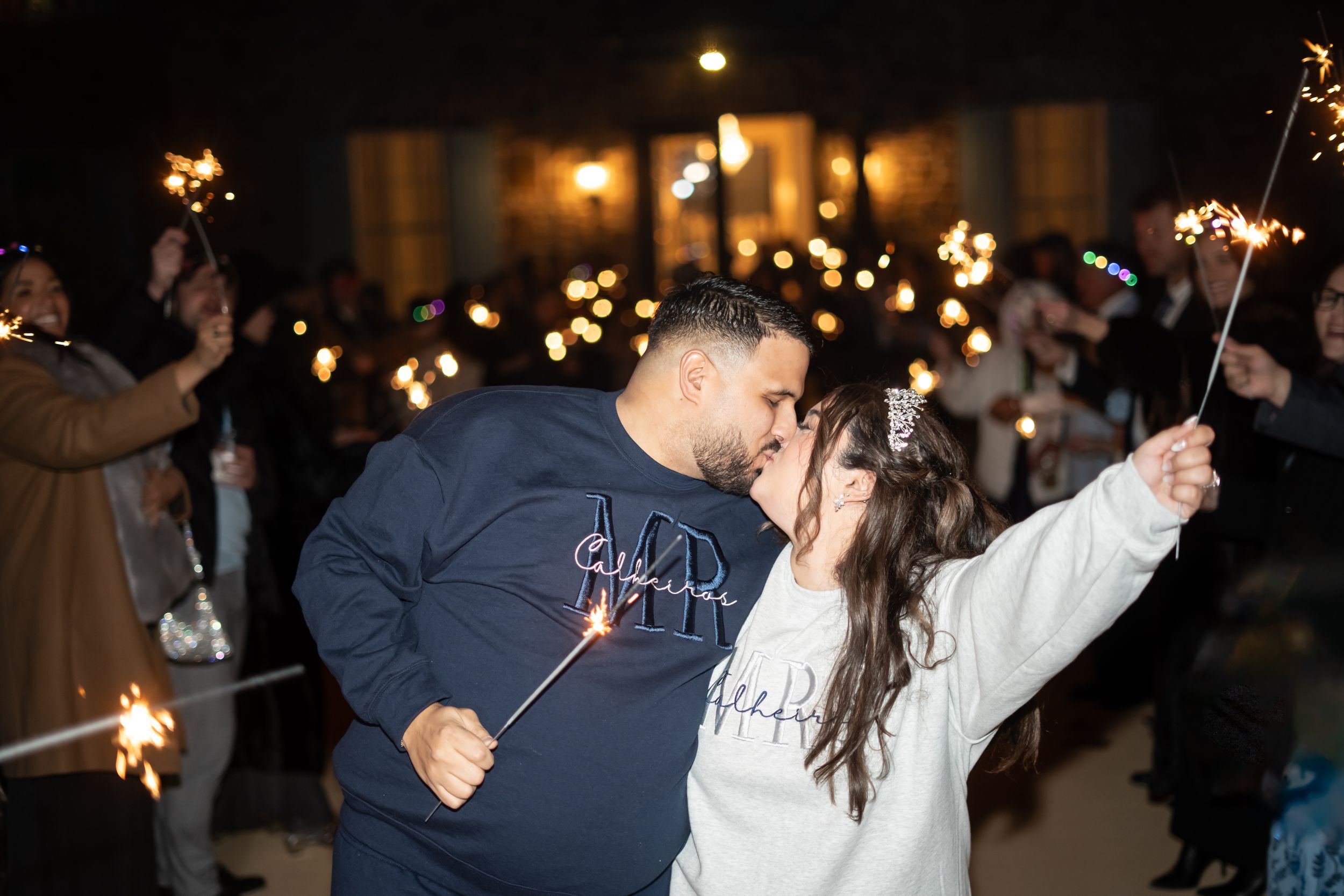 Couple celebrates with sparklers during nighttime wedding festivities.
