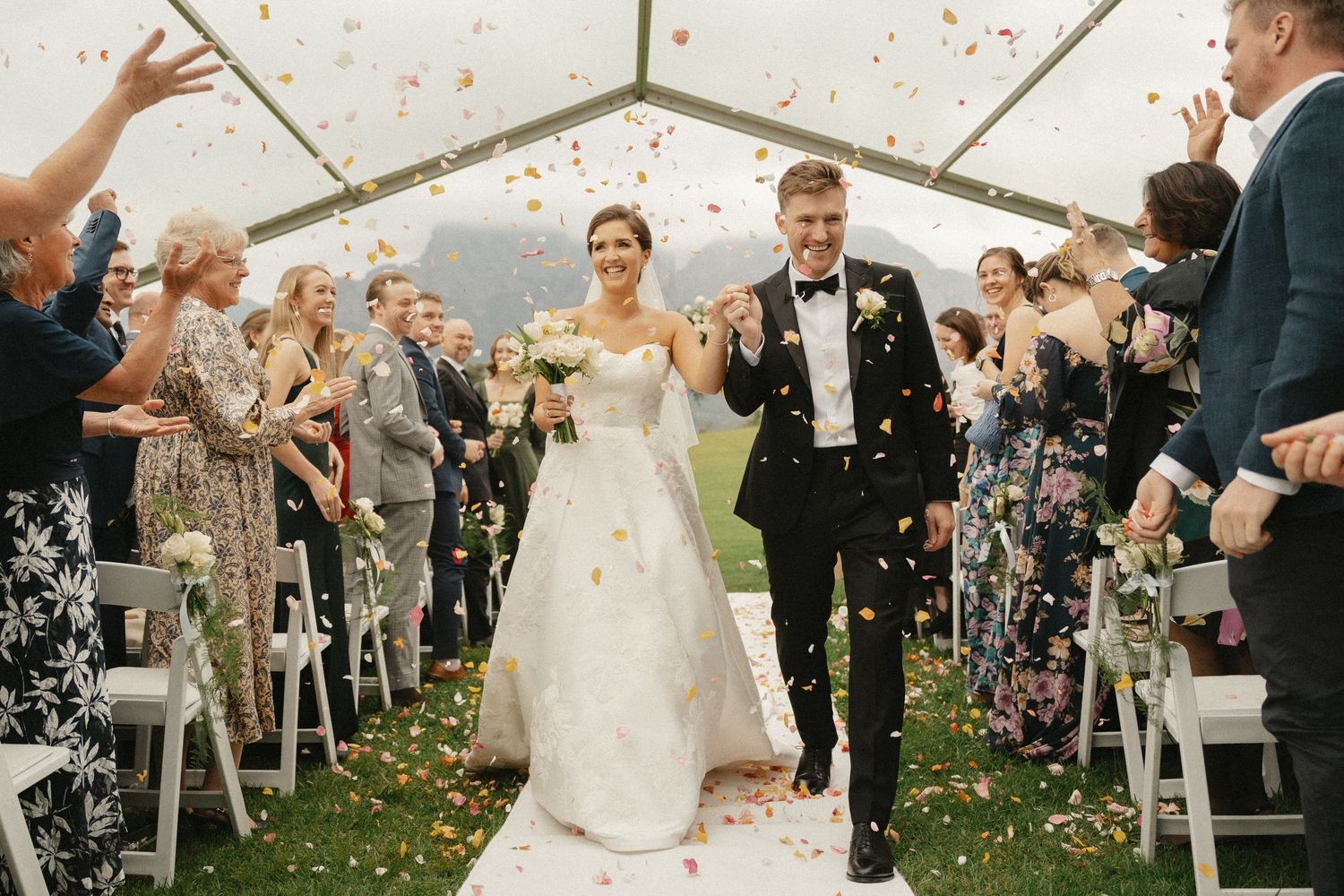 A couple walks hand in hand across a scenic mountain meadow on their wedding day.