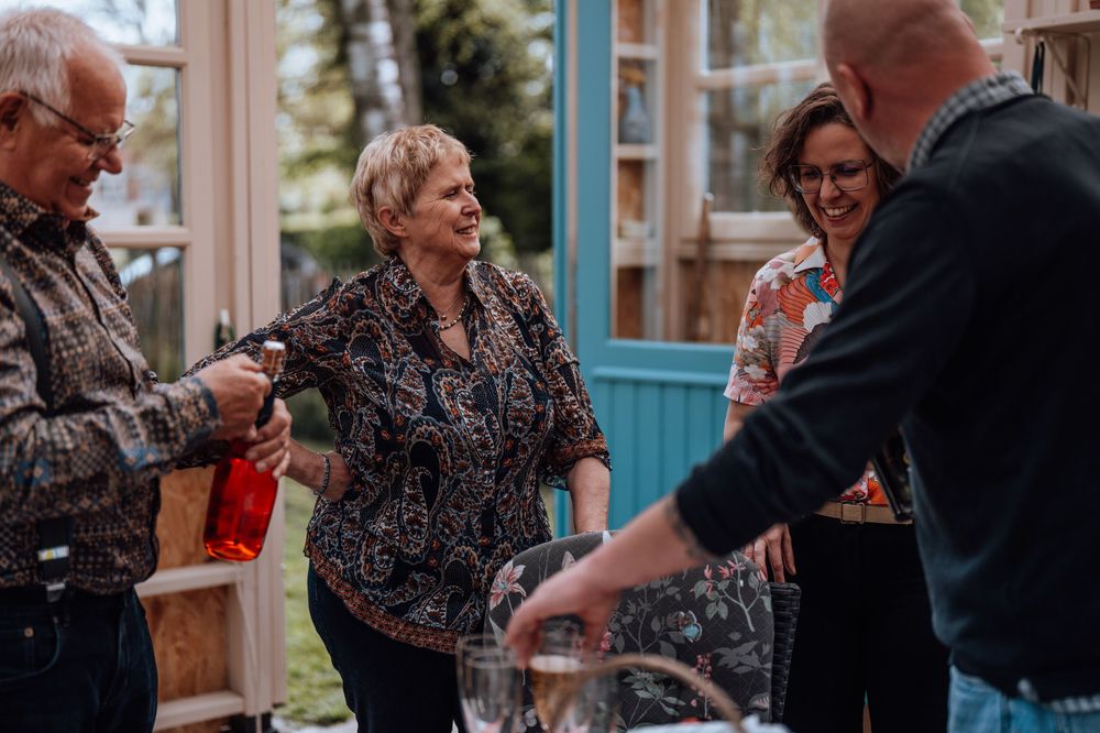 Een gezin die samen lachen terwijl ze bij elkaar zitten met een drankje in de serre van opa