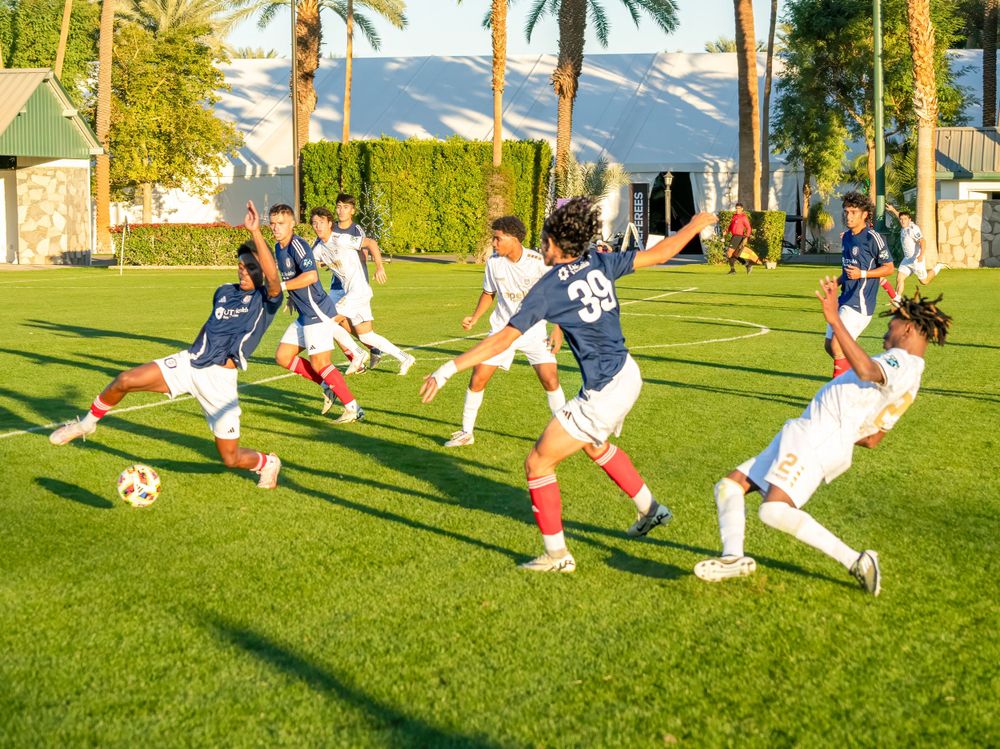 Youth soccer players in action on a sunny field with palm trees in the background.
