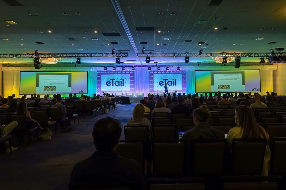 Large conference hall with eTail branding and colorful stage lighting during a presentation.