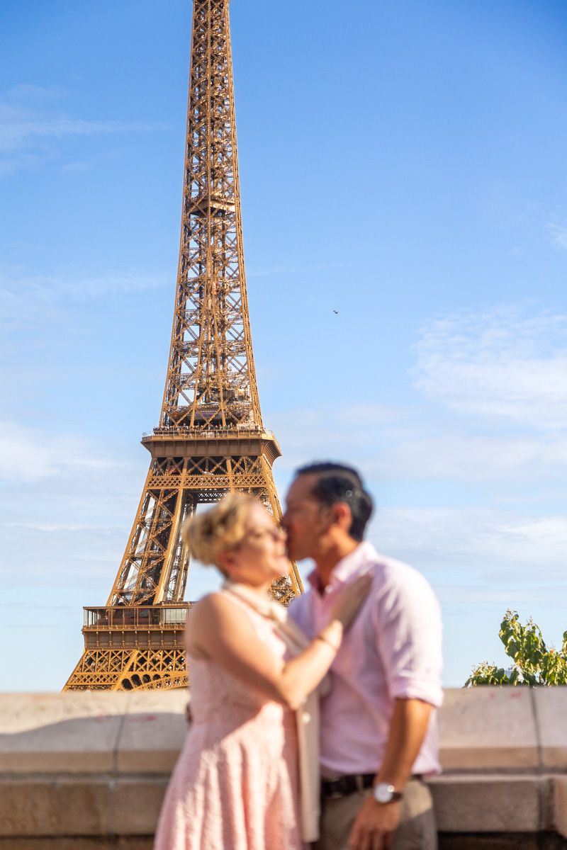 The Eiffel Tower stands tall against a blue sky with a blurred couple in the foreground.