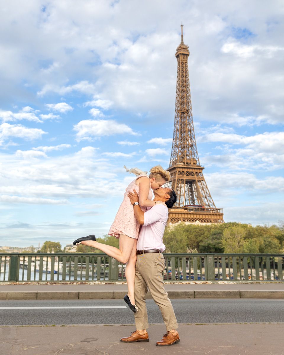 A romantic scene with a pink dress and white shirt in front of the Eiffel Tower against a blue sky.