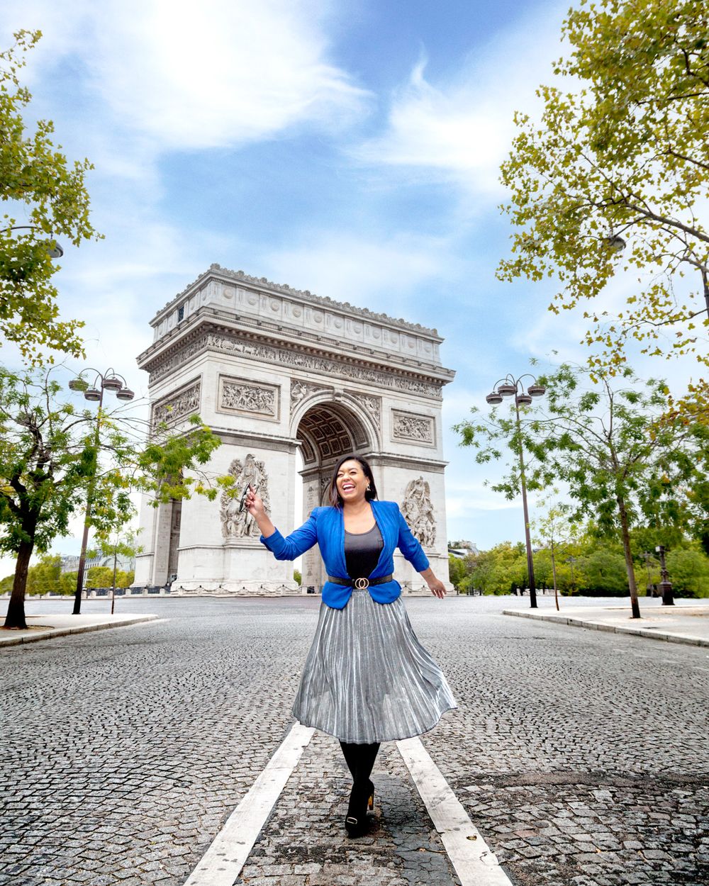 Standing in front of the Arc de Triomphe in Paris wearing a blue jacket and pleated skirt on a spring day.