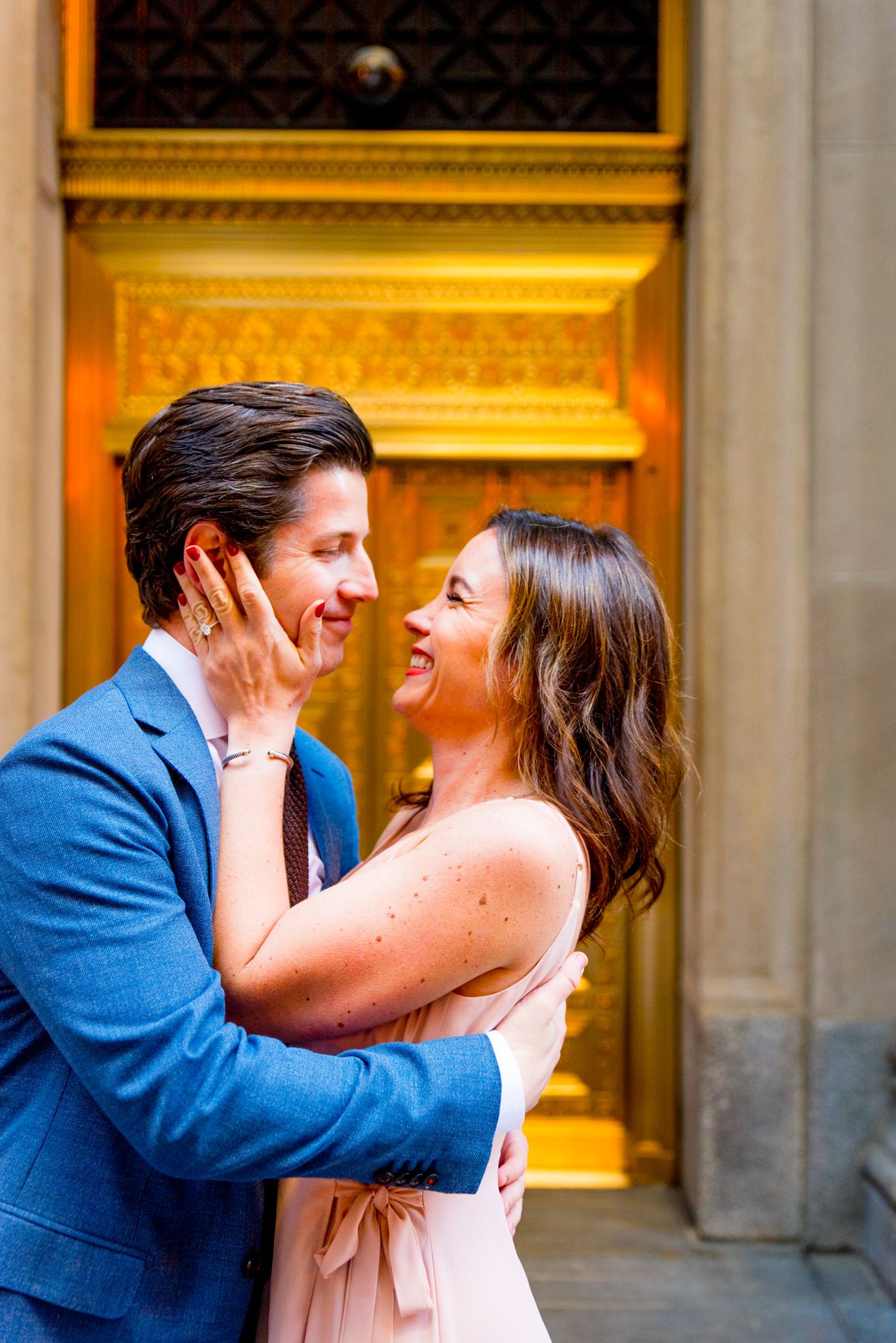 woman holds man's face and they both smile and laugh in front of gold door in downtown Chicago