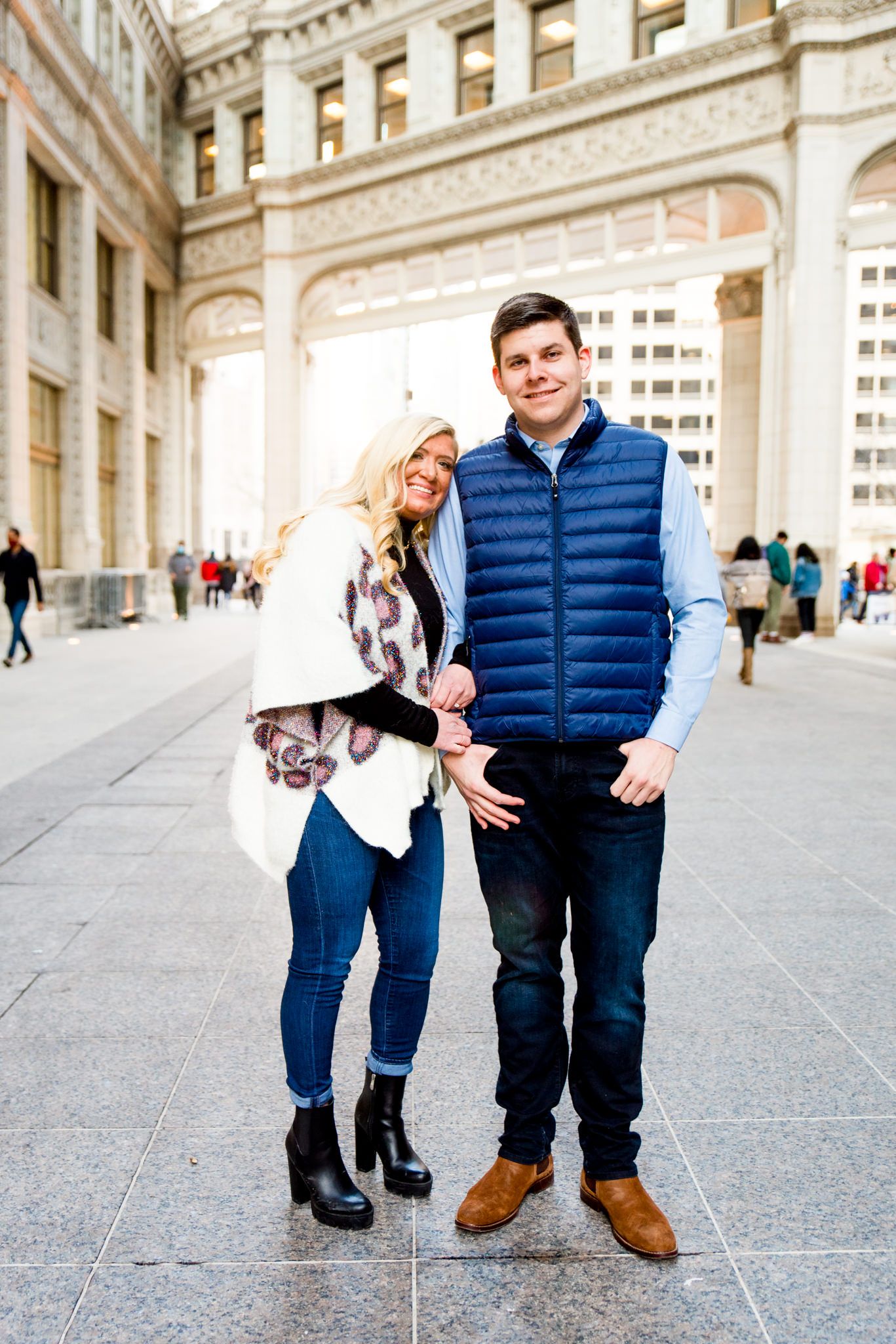 blonde woman in leopard cardigan standing with fiance in blue vest in front for Wrigley Building engagement pictures