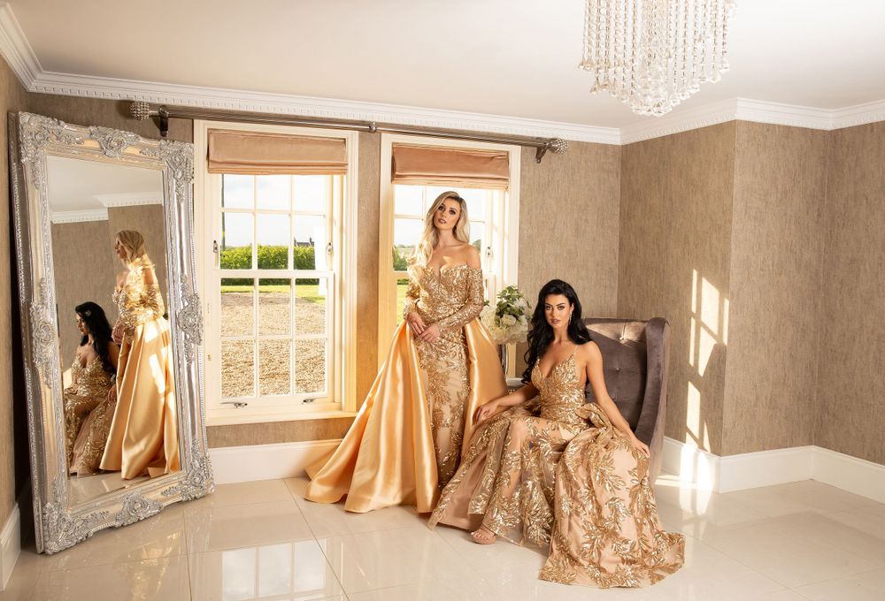 two models wearing gold dresses posed on chairs